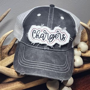 May include: A distressed gray baseball cap with a white mesh back. The front features the word "Chargers" in a white, distressed patch with black and red accents. White stitching details the brim and crown.