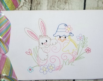 May include: Embroidered design of a bunny and a chick peeking out of an egg, surrounded by flowers. The design is done in a variety of colors, including pink, blue, yellow, and green.