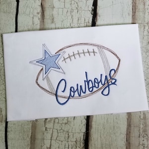 May include: Embroidered design of a football with a blue star and the word "Cowboys" in blue cursive lettering.