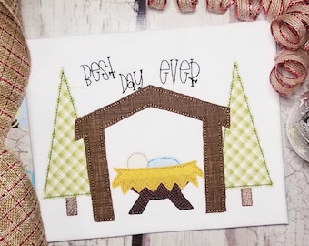 May include: A white background with a brown manger, two green trees, and the text "Best Day Ever". The manger has a yellow hay bed with a blue and white baby inside.