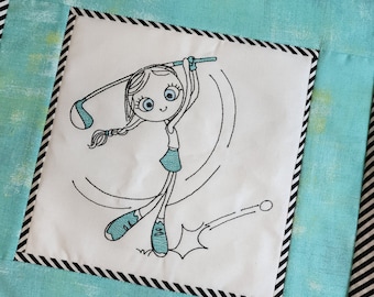 May include: A square, quilted golf-themed wall hanging. The central white square features an embroidered cartoon girl swinging a golf club. The design includes teal and black accents, with a black and white striped border.