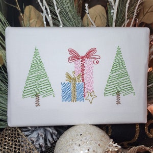 May include: Embroidered white fabric with two green Christmas trees and a pink and blue gift box with a red bow. The gift box is decorated with a gold star.