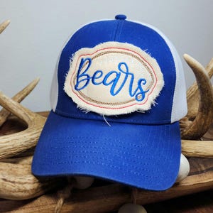 Pode incluir: Boné de caminhoneiro azul e branco com a palavra "Bears" bordada em um patch. O patch tem um fundo creme com uma borda costurada marrom e detalhes vermelhos. O boné tem uma aba curva.