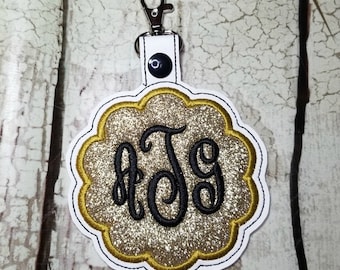 May include: Gold glitter keychain with a black monogram "JTG" in a scalloped circle.