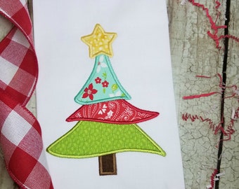 May include: A colorful patchwork Christmas tree applique with a yellow star on top. The tree is made of green, red, blue, and white fabric.