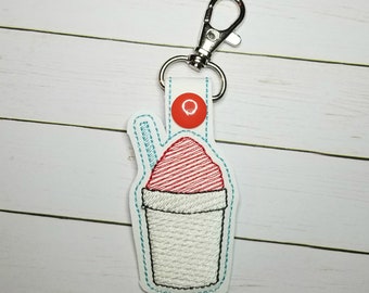Può includere: Un portachiavi ricamato bianco e rosso a forma di cono gelato con una cannuccia blu. Il portachiavi ha un moschettone in metallo argentato.