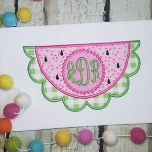 May include: A pink and green watermelon-shaped embroidery design with a scalloped edge. The design features a monogram "ADR" in a circle in the center of the watermelon.
