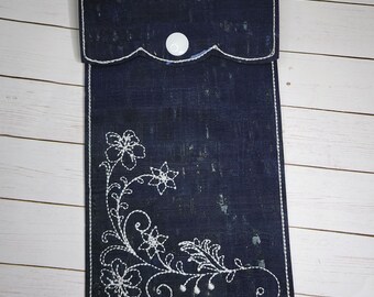 May include: A dark blue fabric pouch with a white button closure and a white floral embroidery design. The pouch is made of a textured material.