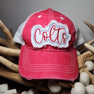 May include: Red and white trucker hat with a distressed look. The hat has a white mesh back and a red front with a white embroidered patch that says "Colts".
