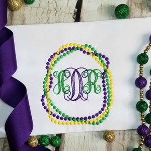 May include: A white fabric with a purple, green, and yellow beaded circle monogrammed with the letters "KOR".