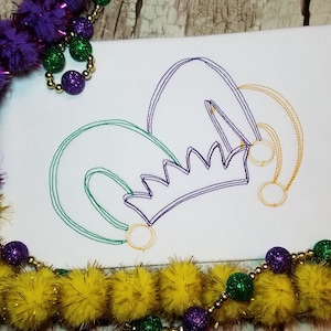 May include: A purple, green, and gold embroidered design of a jester's hat on a white fabric background.
