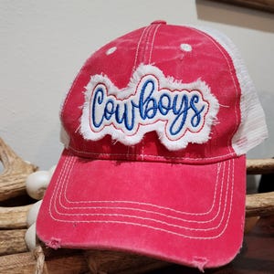 Pode incluir: Boné de beisebol vermelho desgastado com parte traseira em malha branca. A palavra "Cowboys" é bordada em azul em um patch branco na frente. O boné tem uma aba curva e um visual desgastado.