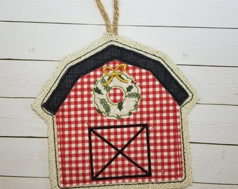 Könnte beinhalten: Rotes und weißes Gingham-Scheunen-Ornament mit schwarzem Dach und einem grünen Kranz mit einer gelben Schleife. Das Ornament hat einen Jute-Rand und einen Jute-Aufhänger.
