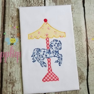 May include: A white fabric applique of a carousel horse with a blue and white floral pattern. The horse is on a red and white checked pole with a yellow and white floral canopy.