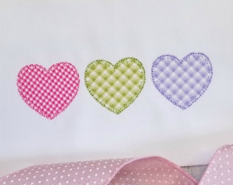 May include: Three embroidered hearts in pink, green, and purple gingham patterns. The hearts are stitched onto a white fabric background.