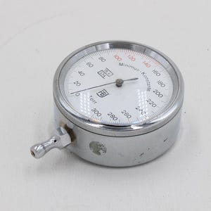 Puede incluir: Un manómetro redondo y plateado con una esfera blanca y marcas negras y rojas. Tiene una pequeña boquilla curva en el lateral y una aguja que indica la presión. El dispositivo está diseñado para medir la presión en bares y kPa.