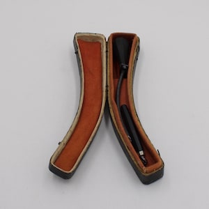 May include: An open, vintage pen case with a black pen inside. The case is black with a brown interior and a curved design. The pen is black and appears to be a fountain pen.