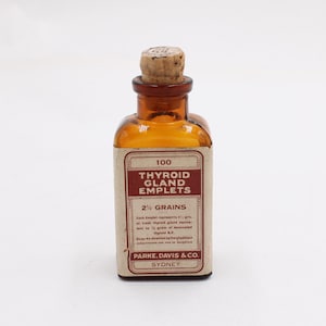 May include: An amber-colored glass bottle with a cork stopper. The bottle has a rectangular label with the text "100 Thyroid Gland Emplets 2 1/2 Grains" and the brand "PARKE, DAVIS & CO. SYDNEY".
