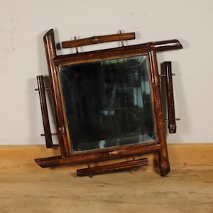 Puede incluir: Un espejo cuadrado con un marco de bambú marrón oscuro. El marco tiene un diseño geométrico único con piezas de bambú horizontales y verticales. El espejo está sobre una pared neutra y una superficie de madera.