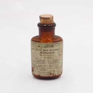 May include: A small, antique brown glass bottle with a cork stopper. The label reads "TABLOID" Iron and Arsenic Compound, with additional text detailing the contents and usage. The bottle is likely from the early 20th century.