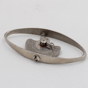 Könnte beinhalten: Ein silberfarbenes Armband mit ovaler Form. Das Armband hat ein dekoratives Mittelelement mit detailliertem Muster. Das Metall hat ein leicht gealtertes Aussehen. Wahrscheinlich aus Silber.