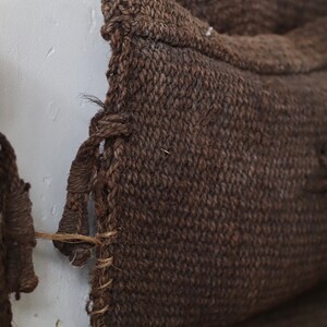 May include: Close-up of a brown woven cushion with a frayed edge. The cushion is made of a coarse, natural fibre.