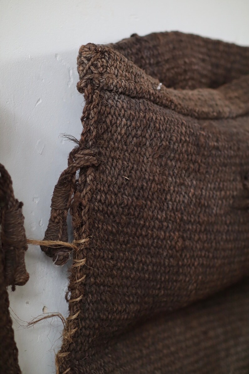 May include: Close-up of a brown woven cushion with a frayed edge. The cushion is made of a coarse, natural fibre.