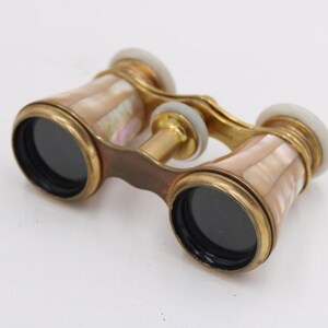 May include: Vintage opera glasses with a gold-tone frame and mother-of-pearl accents. The binoculars have black lenses and white end caps. A classic accessory for theater or events.