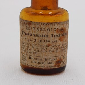 Puede incluir: Una antigua botella de vidrio &aacute;mbar con una etiqueta de papel. La etiqueta dice "TABLOID Potassium Iodide gr. 3 (0,194 g)" e incluye instrucciones de uso. La botella es probablemente de principios del siglo XX.