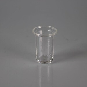 May include: A clear, cylindrical glass vial with a rounded base and a slightly flared rim. The vial is transparent, allowing a view of the interior. The vial is likely used for storing or dispensing liquids or small items.