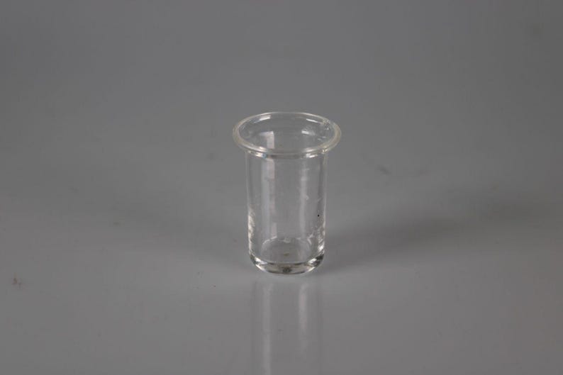 May include: A clear, cylindrical glass vial with a rounded base and a slightly flared rim. The vial is transparent, allowing a view of the interior. The vial is likely used for storing or dispensing liquids or small items.