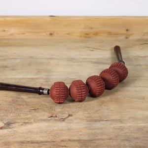 Könnte beinhalten: Ein Vintage-Massagegerät mit sechs roten, strukturierten Rollen, die an einem dunklen Holzgriff befestigt sind. Die Rollen sind in einer gebogenen Linie angeordnet und dienen zur Muskelentspannung. Der Griff ist ebenfalls aus dunklem Holz.