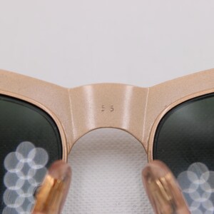 May include: Close-up of sunglasses with a light brown frame and dark lenses. The bridge of the sunglasses has the number "55" printed on it. The temples are a light brown color.