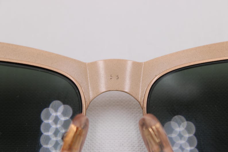 May include: Close-up of sunglasses with a light brown frame and dark lenses. The bridge of the sunglasses has the number "55" printed on it. The temples are a light brown color.