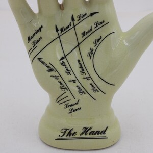 May include: A pale yellow ceramic hand figurine with black lines and text indicating palmistry features. The base reads "The Hand". Lines include "Marriage Lines", "Heart Line", and "Life Line".