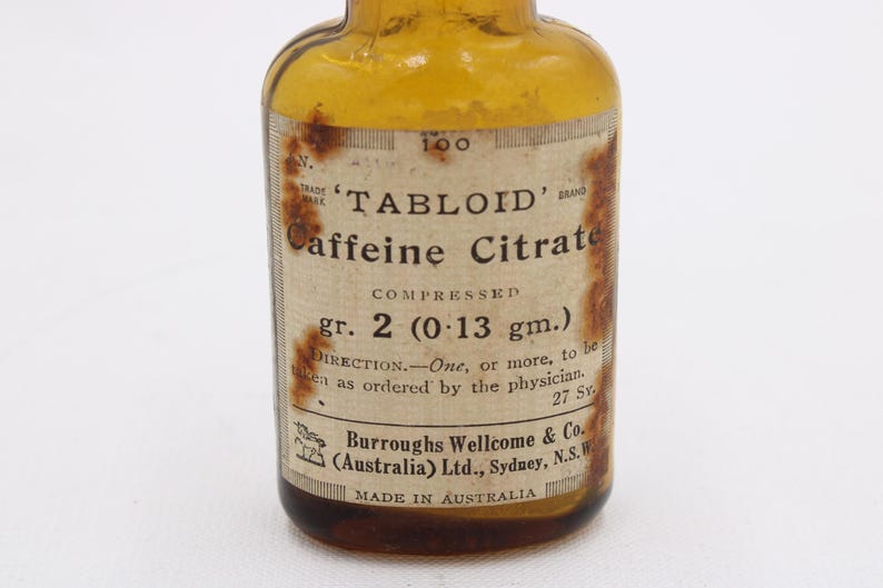 May include: An old amber glass bottle with a label stating "TABLOID Caffeine Citrate." The label details the dosage, "gr. 2 (0.13 gm.)", and the manufacturer, Burroughs Wellcome & Co., Made in Australia. The bottle is a vintage pharmaceutical item.