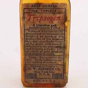 May include: An antique amber glass bottle with a paper label. The label reads "Trypsogen" and details the contents as a digestive and antiglycosuric tablet. The bottle is marked "Made in U.S.A."