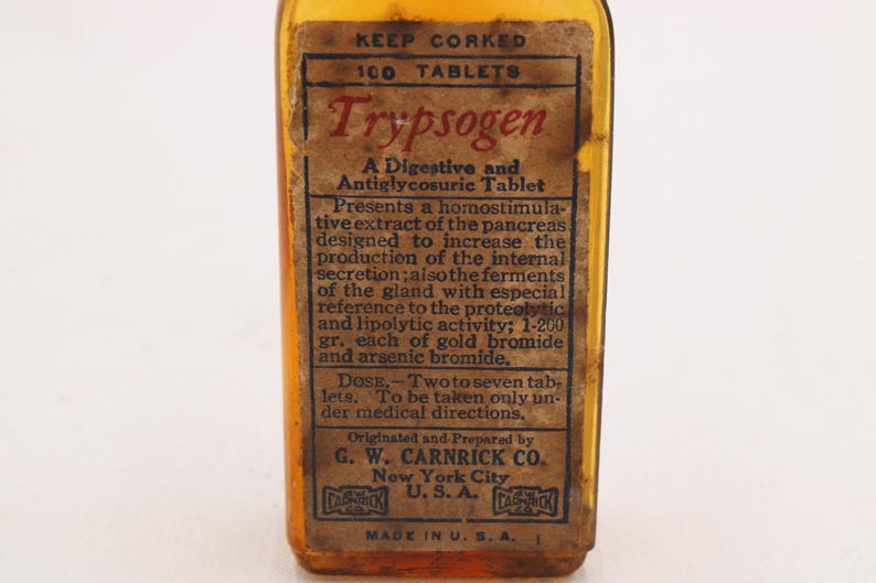 May include: An antique amber glass bottle with a paper label. The label reads "Trypsogen" and details the contents as a digestive and antiglycosuric tablet. The bottle is marked "Made in U.S.A."