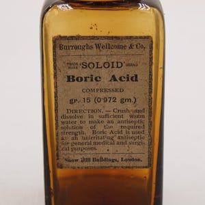 May include: An antique amber glass bottle with a label reading "Boric Acid." The label also includes the text "SOLOID" and "Burroughs Wellcome & Co." The bottle contains compressed boric acid, gr. 15 (0.972 gm.).