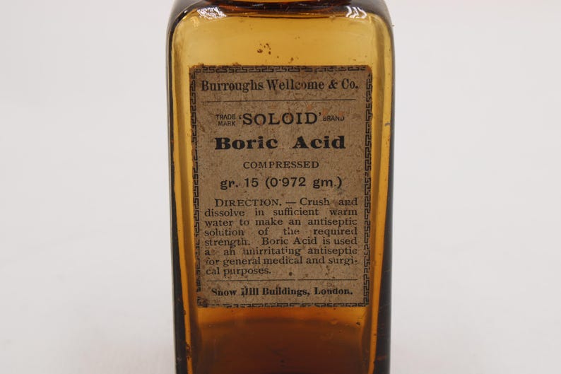May include: An antique amber glass bottle with a label reading "Boric Acid." The label also includes the text "SOLOID" and "Burroughs Wellcome & Co." The bottle contains compressed boric acid, gr. 15 (0.972 gm.).