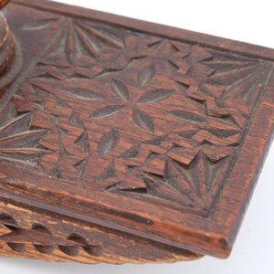May include: Close-up of a vintage wooden inkwell with intricate carved floral and geometric patterns. The inkwell is a rich brown color, showcasing detailed craftsmanship and a classic design.