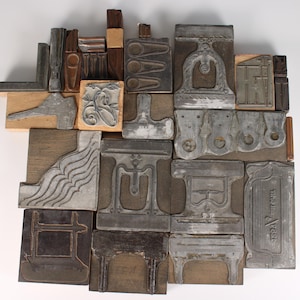 Può includere: Una collezione di blocchi di stampa vintage di varie forme e dimensioni. I blocchi sono realizzati in metallo e legno, con disegni e motivi intricati. Alcuni blocchi presentano elementi architettonici, altri motivi decorativi.