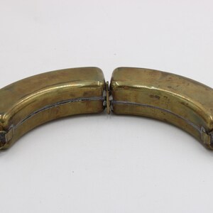 May include: Two-part brass flask with a curved, banana-like shape. Each half has a screw-on cap made of a silver-colored metal. The flask is designed to be separated into two pieces. The brass has a slightly aged appearance.