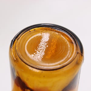 May include: Close-up of the bottom of a brown glass bottle. The bottle has a rounded base with concentric circles and a dark rim. The glass has a glossy, reflective surface.