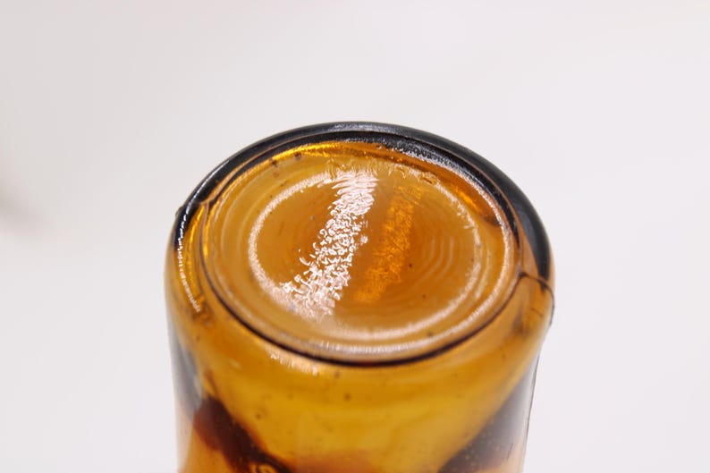 May include: Close-up of the bottom of a brown glass bottle. The bottle has a rounded base with concentric circles and a dark rim. The glass has a glossy, reflective surface.