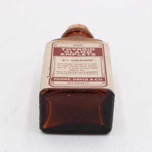 May include: An antique brown glass bottle with a cork stopper. The label reads "Thyroid Gland Emplets" and "2 1/2 Grains" with text from Parke, Davis & Co., Sydney. The bottle is rectangular with rounded corners.