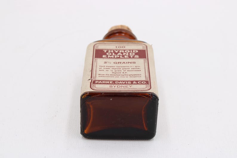 May include: An antique brown glass bottle with a cork stopper. The label reads "Thyroid Gland Emplets" and "2 1/2 Grains" with text from Parke, Davis & Co., Sydney. The bottle is rectangular with rounded corners.