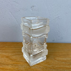 May include: A clear glass vase with a square shape and a textured design. The vase is made of multiple layers of glass, creating a unique and modern look.