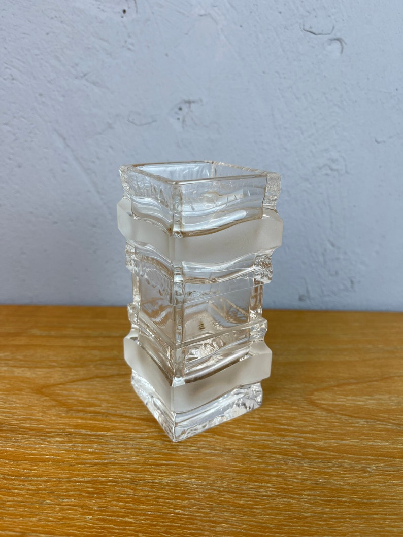 May include: A clear glass vase with a square shape and a textured design. The vase is made of multiple layers of glass, creating a unique and modern look.
