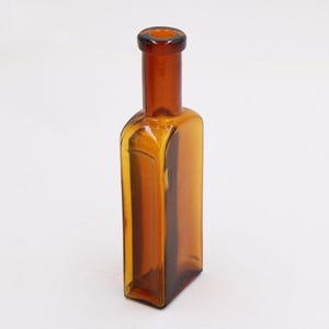 May include: Amber-colored glass bottle with a rectangular body and a narrow neck. The bottle has a vintage aesthetic, with a slightly rounded base and a dark amber hue. The glass appears to be transparent, allowing light to pass through.